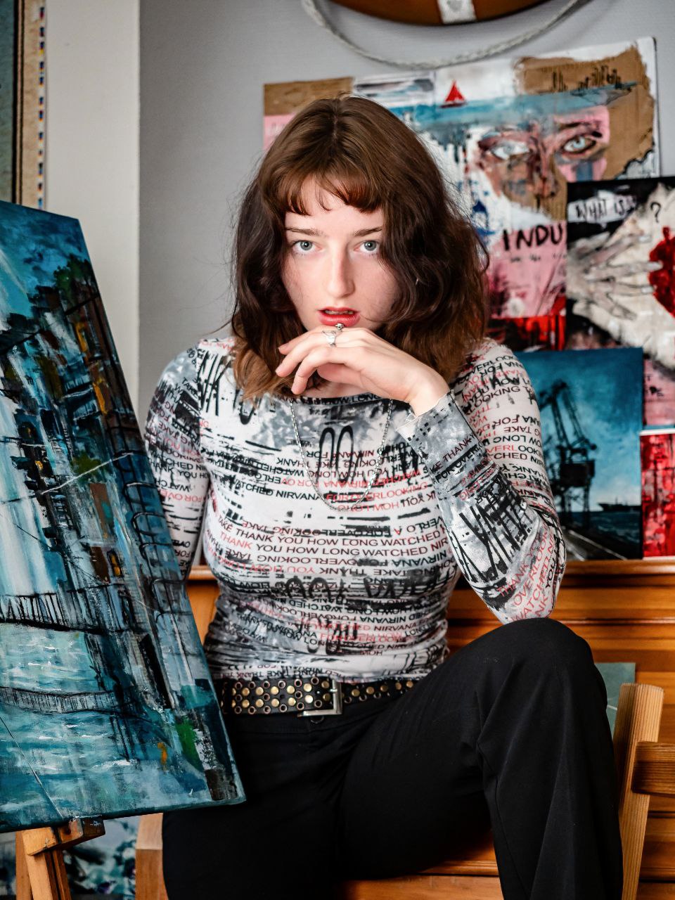 Jeune artiste en pose expressive, entourée de ses œuvres picturales