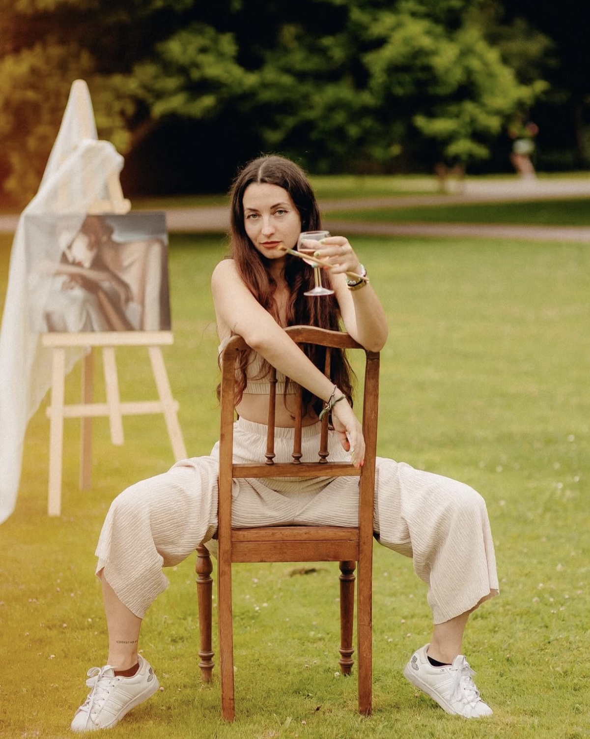 Artiste assise sur une chaise dans un parc, posant devant un chevalet