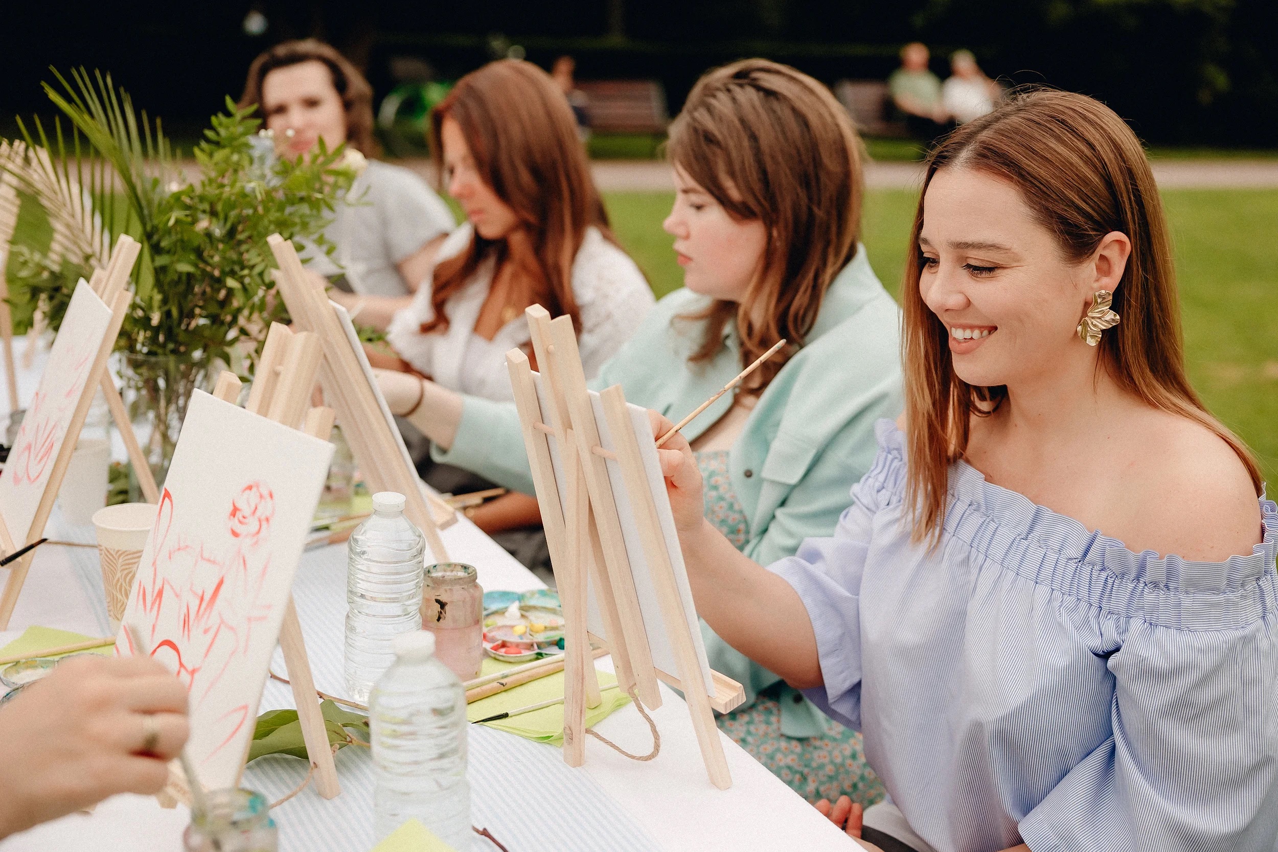 Femmes souriantes concentrées sur leurs toiles lors d’un atelier de peinture en plein air, ambiance conviviale