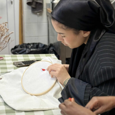 Femme concentrée sur un motif de broderie, travaillant à la main sur tissu tendu dans un tambour à broder