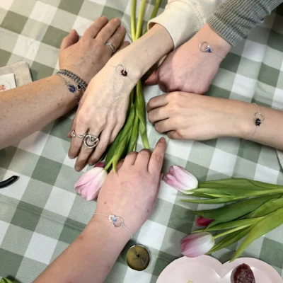 Création de bracelets artisanaux présentés sur les poignets de plusieurs personnes autour de fleurs et d’outils créatifs